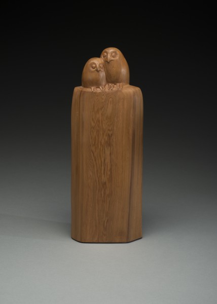 Two owls huddled together on top of a tall wood base