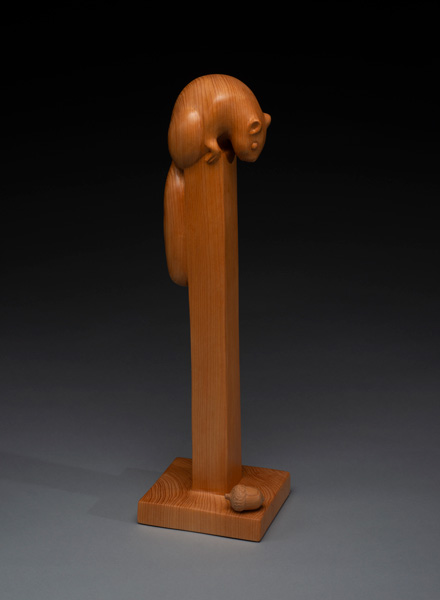sculpture of squirrel on tall post looking down an acorn